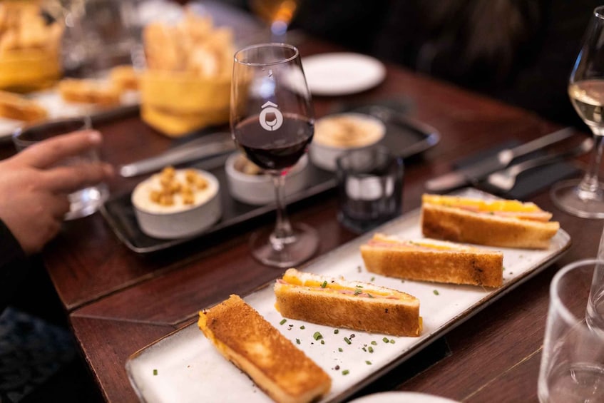 A dining table with a plate of toasted sandwiches, a glass of red wine, and a dessert. 1