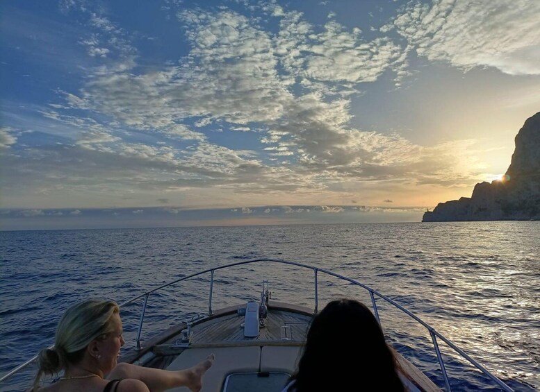A boat on calm waters with a sunset and cliffs in the distance. 2