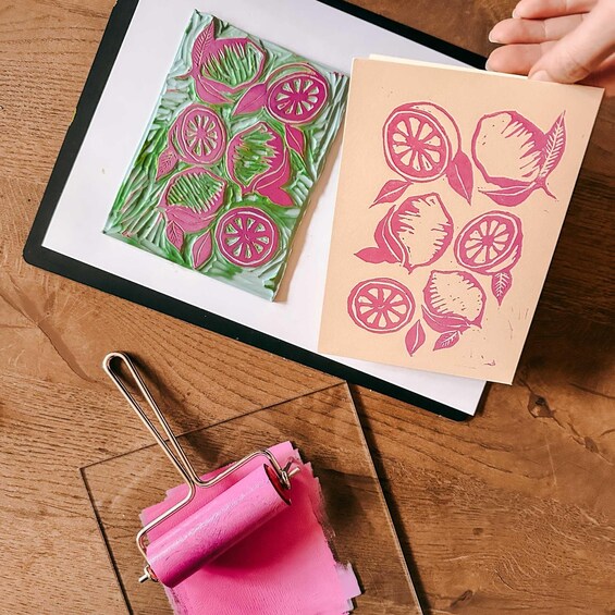 A printed design of citrus slices on a brown paper, a pink clipboard, and a framed print on a wooden table. 3