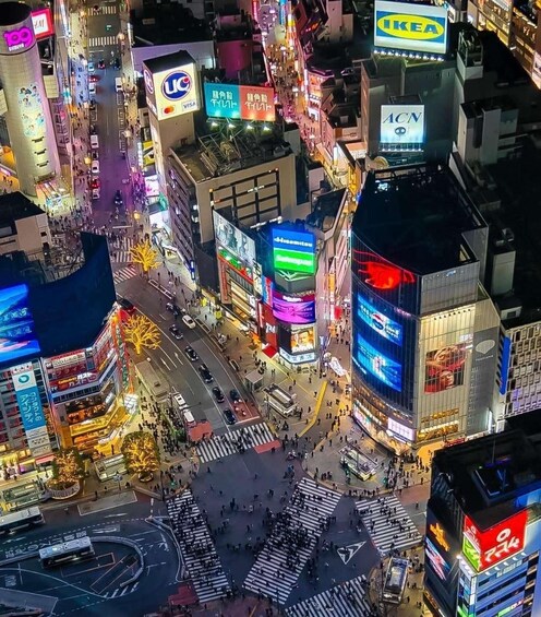 A busy urban intersection with brightly lit commercial buildings and various international brand signs. 1