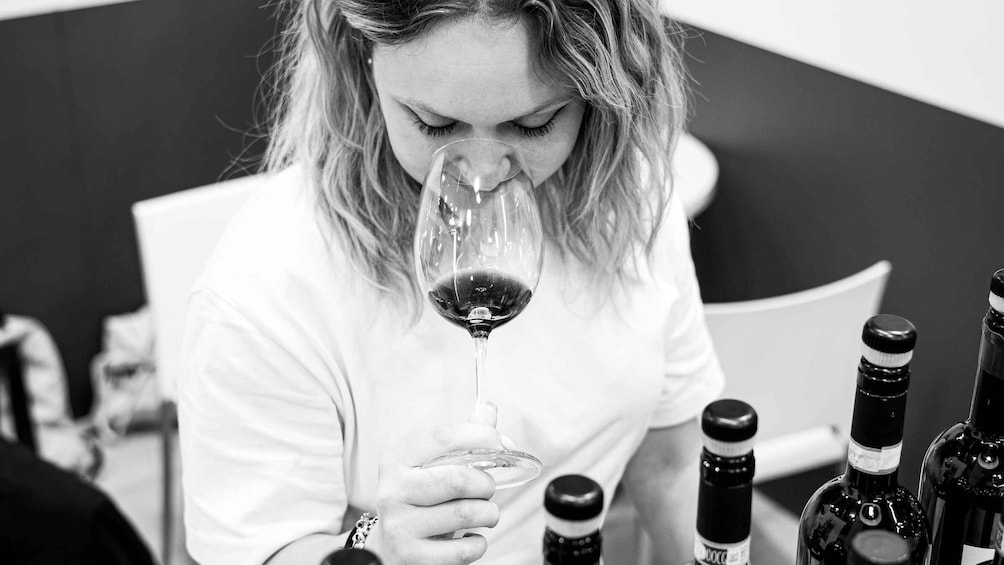 A person holding a wine glass, seated at a table with multiple wine bottles. 1