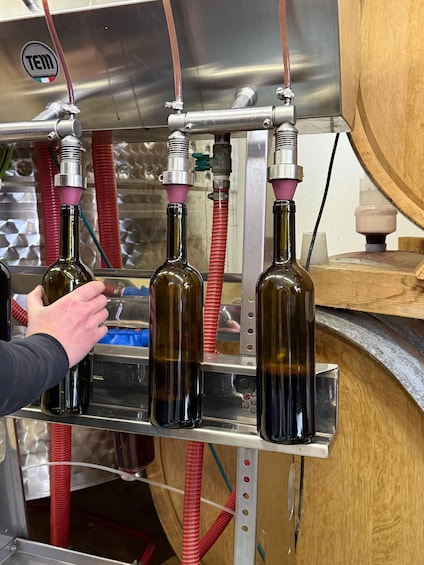 A person handling bottles in a stainless steel environment with red hoses and a logo. 2