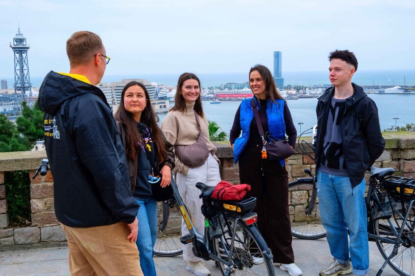 A group of people standing by a waterfront with bicycles and a tall tower in the background. 4