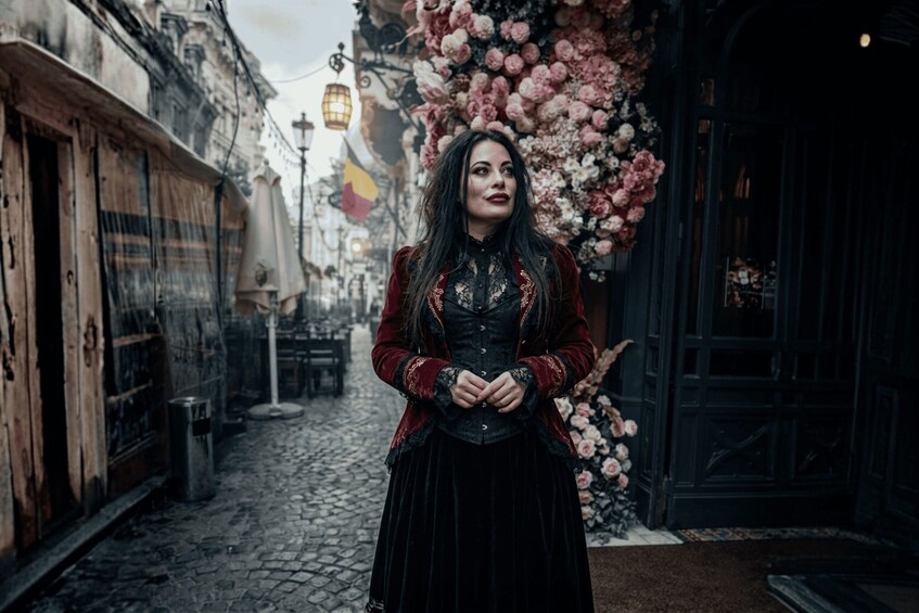 A person standing in a cobblestone street with buildings on either side, a floral arrangement, and a flag. 2