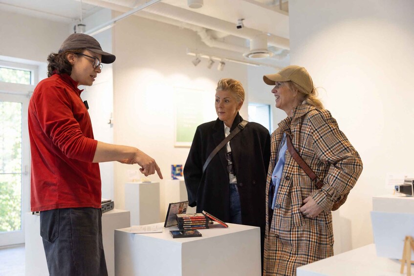 Three people in an art gallery with books and a camera on display. 5
