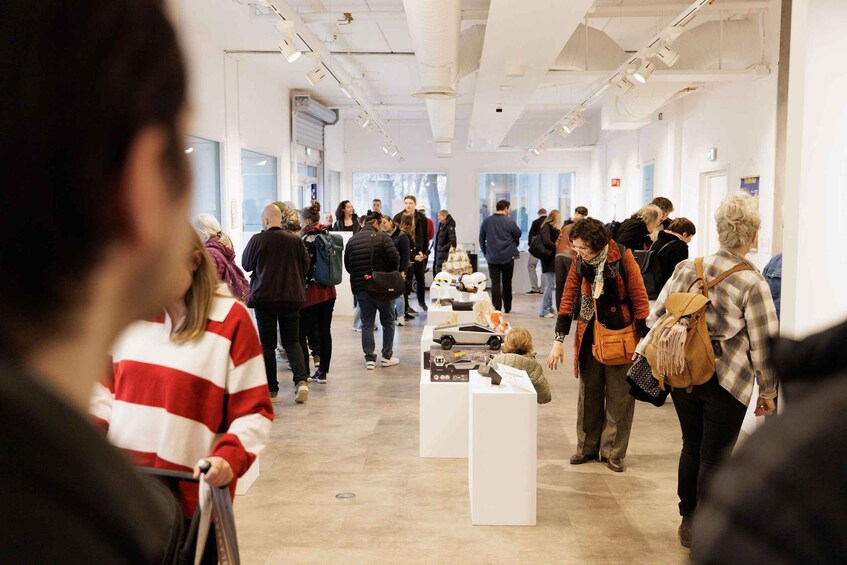 A group of people walking through an art gallery with white walls and ceiling lights. 2