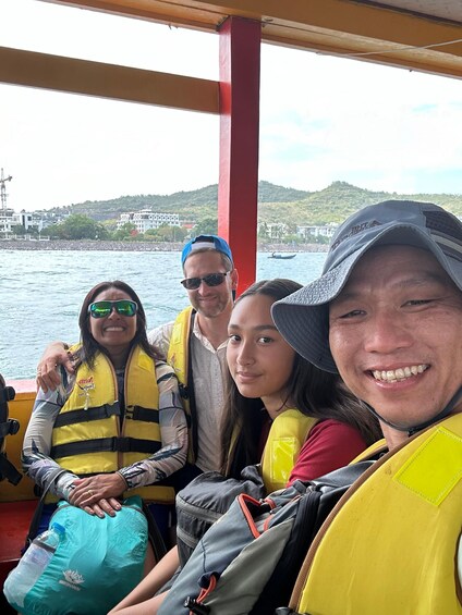 A group of people on a boat with life jackets, a red pillar, and a water body with buildings in the background. 5