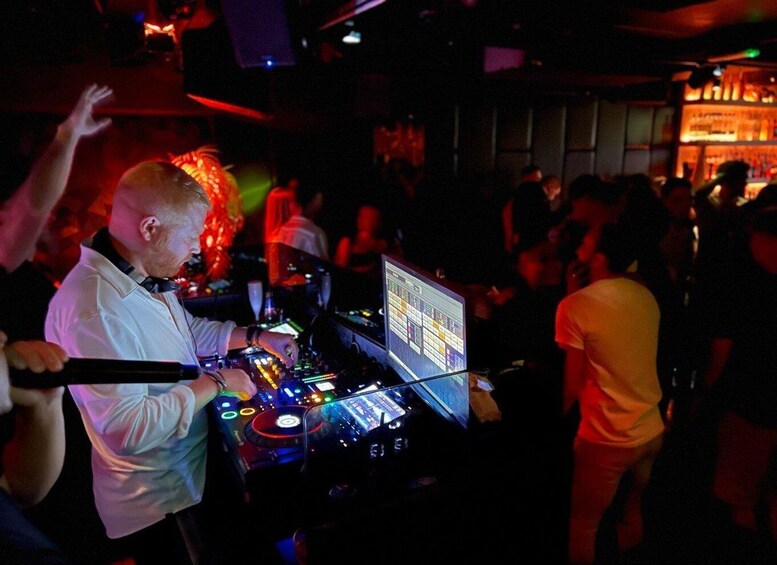 A DJ booth with a laptop and mixing equipment, surrounded by a crowd in a dimly lit venue. 2