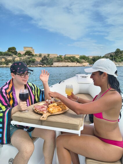 Two people on a boat, one holding a glass of wine and the other holding a glass of juice, with a plate of food in between them. 3