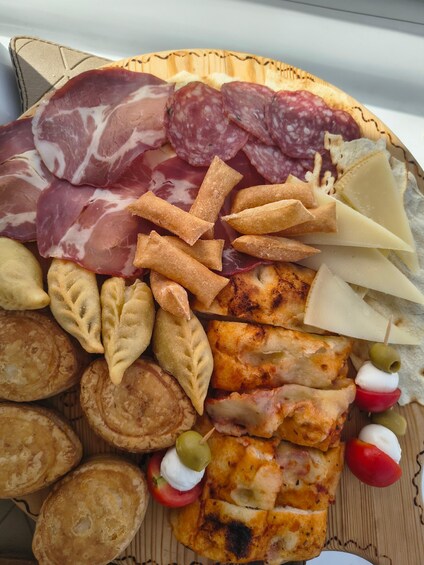 An assortment of cured meats, cheeses, and pastries on a wooden board. 2