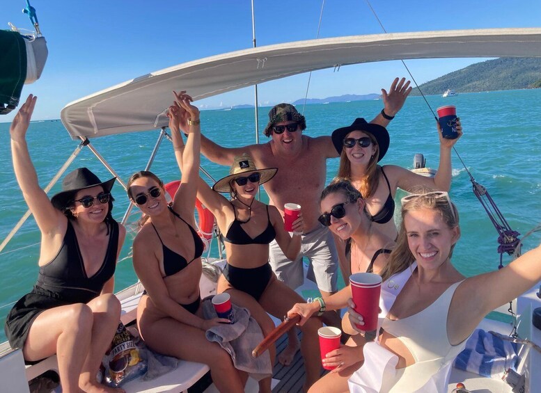 A group of people on a sailboat with drinks and a lifebuoy visible. 1