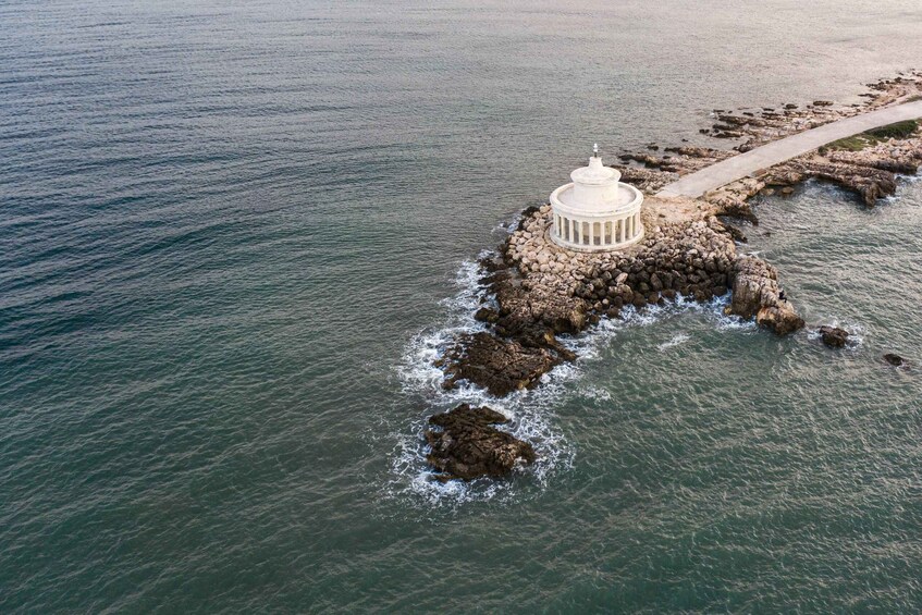 An aerial view of a white lighthouse on a rocky outcrop surrounded by calm sea. 3