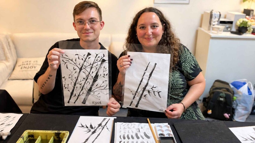 Two people holding artwork with tree branches. 2