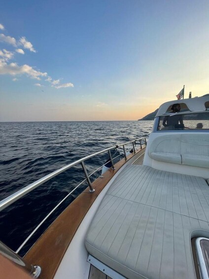 A boat's deck with a railing, a white cushioned area, and a view of the sea and distant land. 3