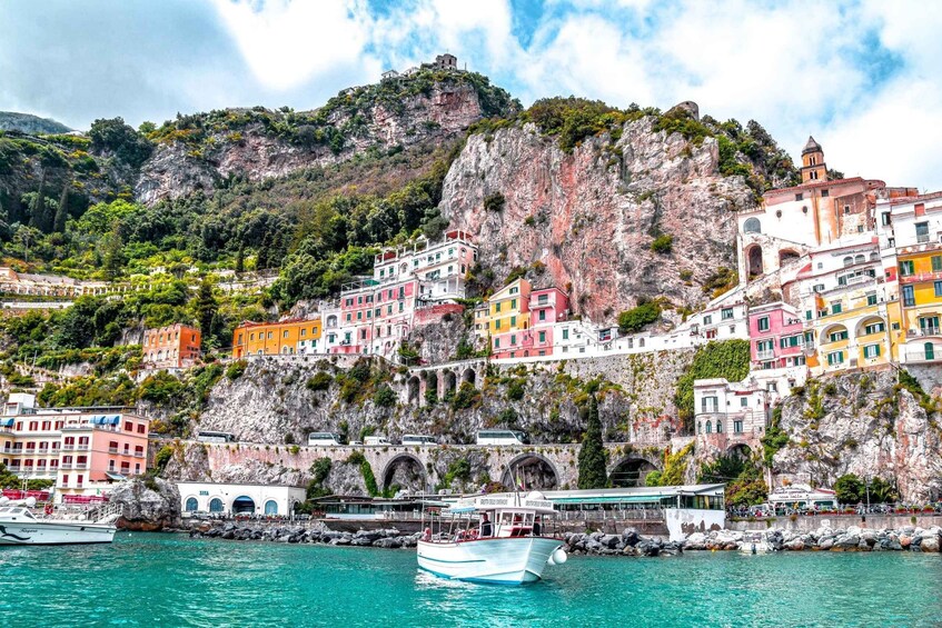 A coastal town with colorful buildings, a rocky cliff, and a boat in the water. 1