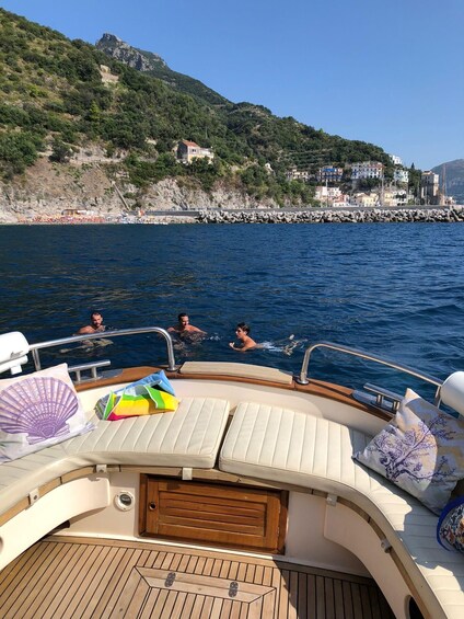A boat with a wooden deck, two lounge chairs, and a view of a rocky coastline with buildings. 5
