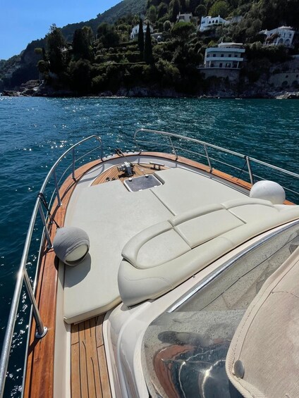 A boat's deck with a wooden floor, cushioned seating, and a view of a coastal area with buildings and greenery. 3