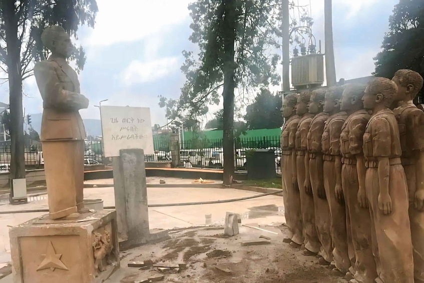 A statue of a man with a star emblem, a row of childlike figures, and a sign with text. 5