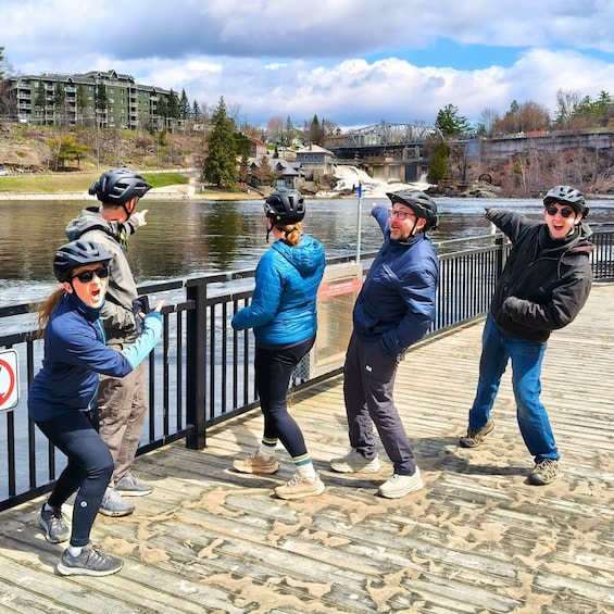 A group of people on a wooden boardwalk by a river, wearing helmets and casual outdoor clothing. 2