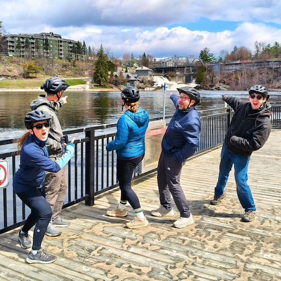 A group of people on a wooden boardwalk by a river, wearing helmets and casual outdoor clothing. 2