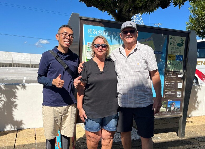 Three people standing in front of a sign with Japanese text and a map. 3