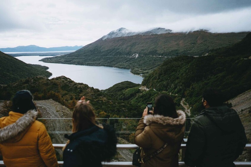 A group of people taking a photo of a lake surrounded by mountains. 4