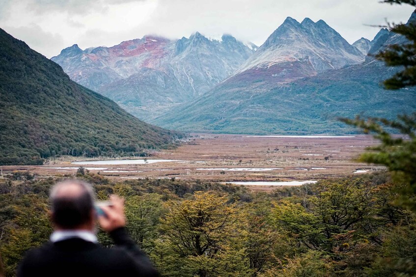 A mountainous landscape with a valley and a person taking a photo. 1
