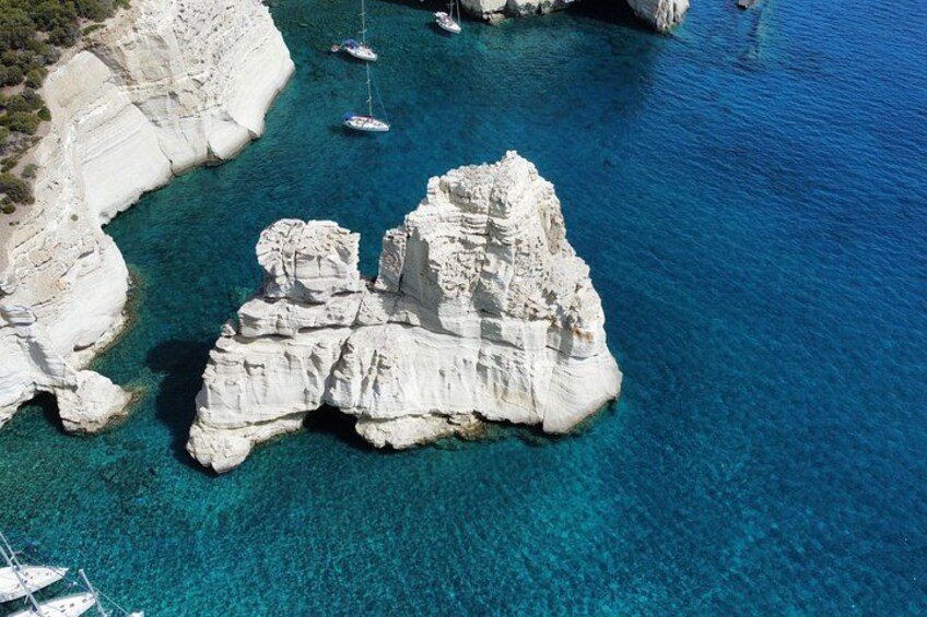 Una costa rocciosa con acque turchesi cristalline e imbarcazioni ancorate nelle vicinanze. 5