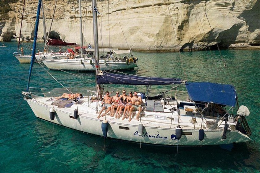 Un velero llamado 'A. Kairis' con gente a bordo, anclado cerca de acantilados rocosos en aguas azul turquesa. 3