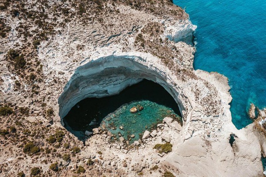 Paesaggio costiero con una grande formazione a grotta circondata da terreno roccioso e acque cristalline. 2