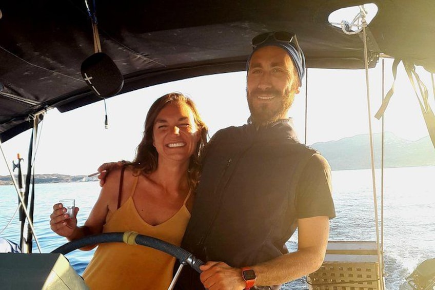 Una embarcación con dos personas, una manejando el timón, y un mar tranquilo al fondo. 4
