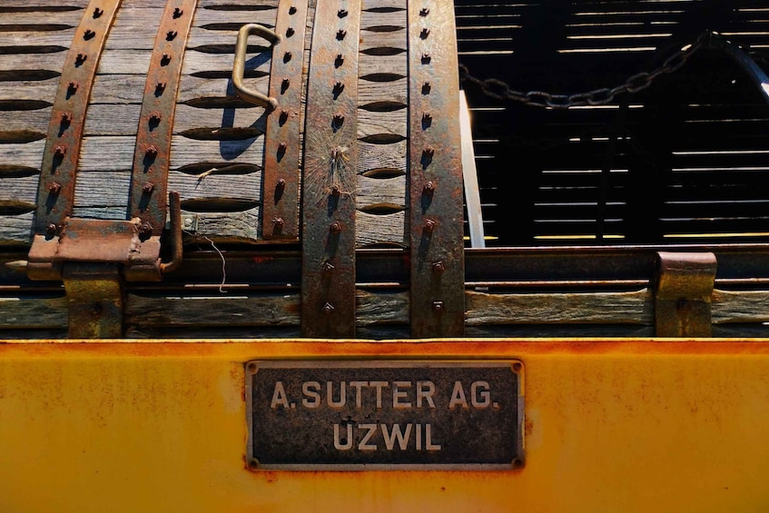 A rusty metal structure with a yellow base and a sign reading 'A. SUTTER AG. UZWIL'. 2