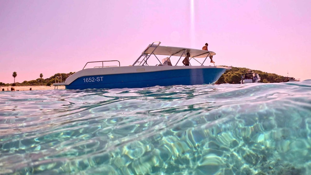 A blue boat with the number 1652-ST on its side, floating on clear water with a beach and palm trees in the background. 5