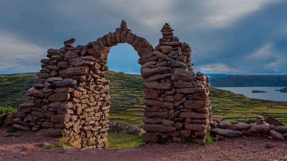 A stone archway in a rural landscape with terraced fields and a lake in the background. 4