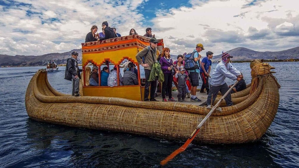 A large, traditional boat with passengers and a guide on a calm lake. 1