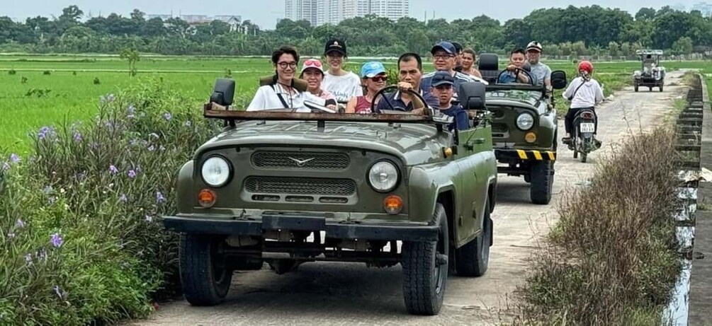 A convoy of military jeeps on a rural road with passengers. 3