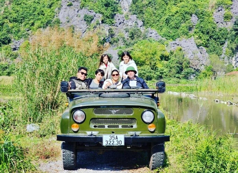 A green jeep with a license plate 35A 322.30, parked by a river with greenery and rocks in the background. 5