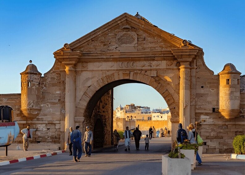 An ancient stone archway with people walking through it. 1