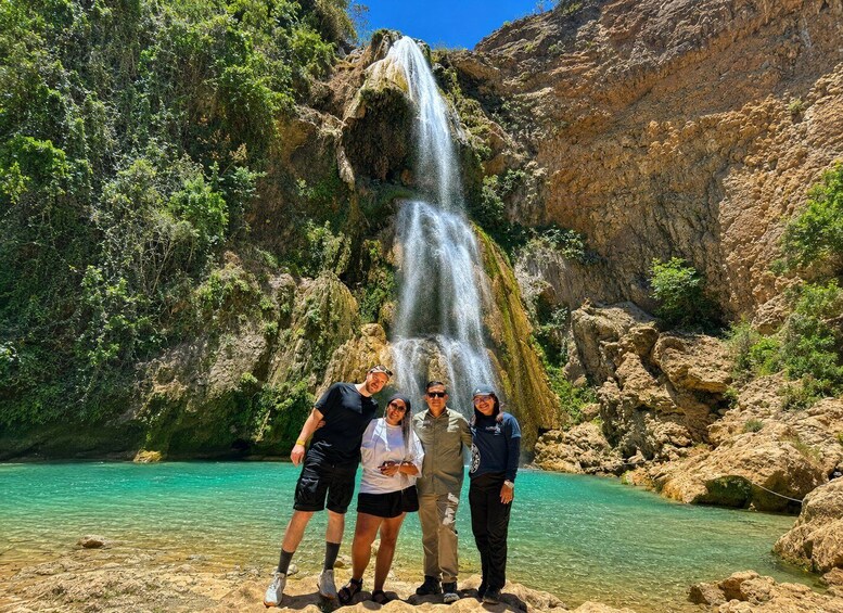 A group of people standing by a waterfall in a rocky canyon with clear turquoise water. 1
