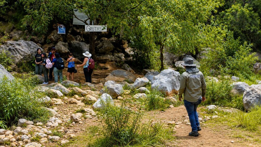 A hiking trail with large rocks and greenery, a sign reading 'GRUTAS,' and a person in a hat walking away. 4