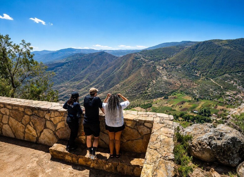 Three people standing on a stone wall overlooking a valley with mountains in the distance. 3