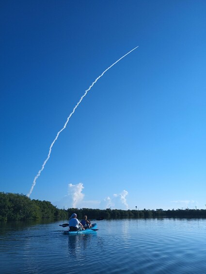 A person kayaking on a calm lake with a clear sky and a contrail from an airplane. 5
