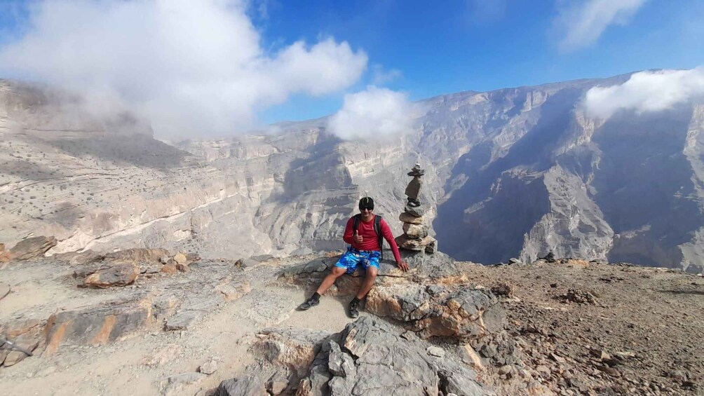 A person sitting on a rocky outcrop with a mountain range in the background. 2