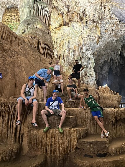 A group of people sitting on rock formations in a cave with stalactites. 4