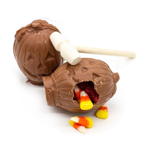 A chocolate-covered confection with a face, a stick, and candy corn pieces. 1