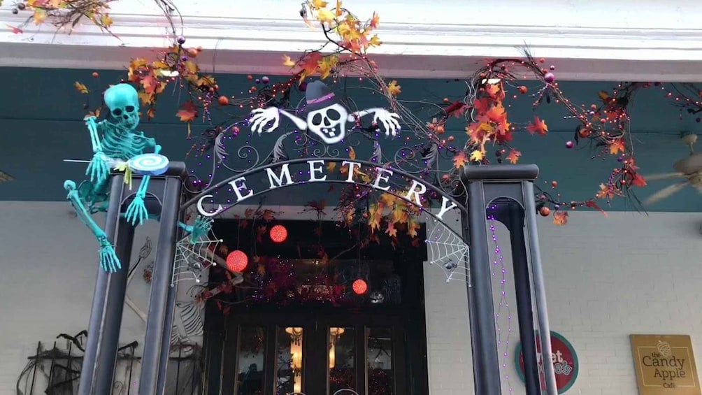 A building entrance with a sign reading 'CEMETERY' and Halloween decorations including a skeleton and autumn leaves. 2