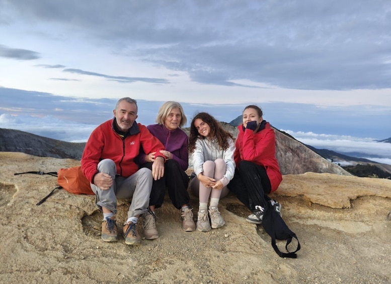 Four people sitting on a rocky outcrop with a mountainous landscape in the background. 3