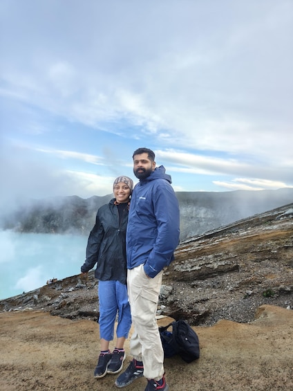 Two people standing on a rocky terrain with a misty lake and mountains in the background. 5