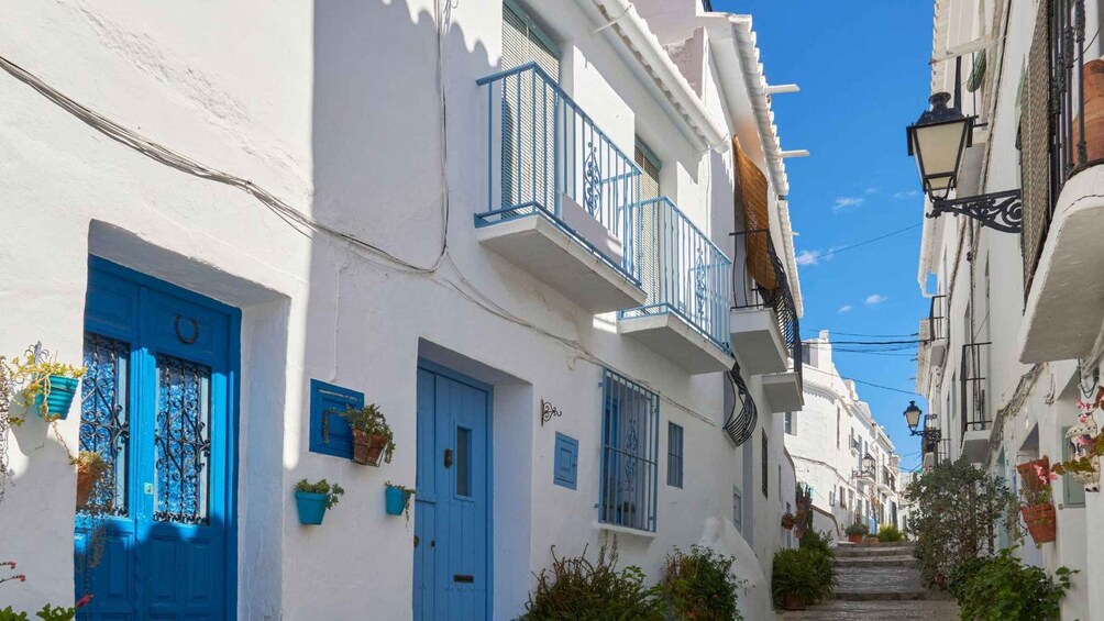 A narrow street with white buildings, blue doors, and balconies. 5
