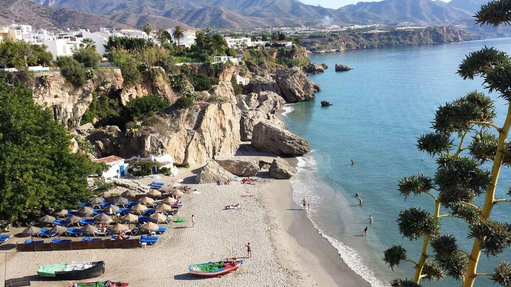 A coastal beach with umbrellas, boats, and rocky cliffs. 4